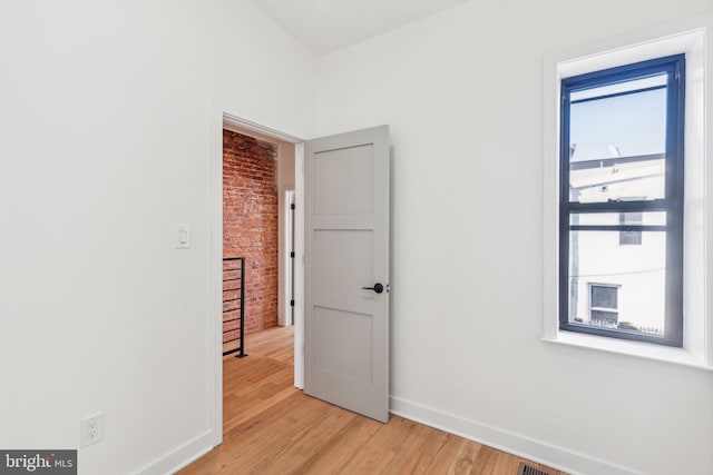 spare room with light wood-type flooring, brick wall, and baseboards