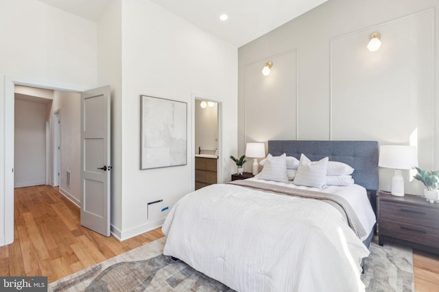 bedroom with light wood-type flooring, high vaulted ceiling, baseboards, and ensuite bathroom