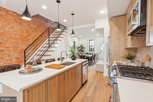 kitchen with stainless steel appliances, light countertops, light wood-style flooring, a sink, and an island with sink