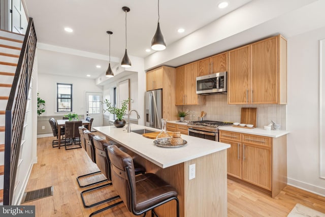 kitchen with light wood finished floors, stainless steel appliances, visible vents, decorative backsplash, and a sink