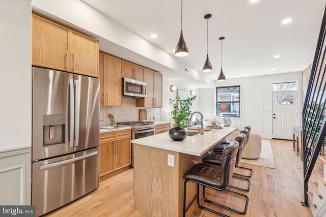 kitchen with tasteful backsplash, an island with sink, light wood-style flooring, stainless steel appliances, and light countertops