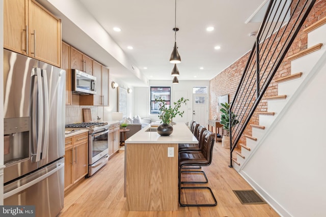 kitchen featuring stainless steel appliances, visible vents, light wood-style floors, light countertops, and a center island with sink