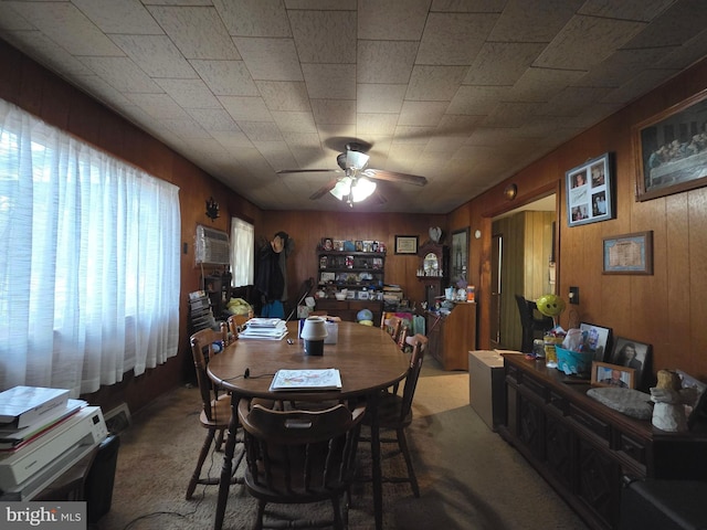 carpeted dining space featuring wood walls and ceiling fan