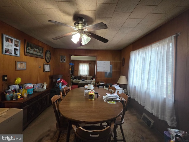 dining room with ceiling fan, wooden walls, visible vents, and carpet flooring