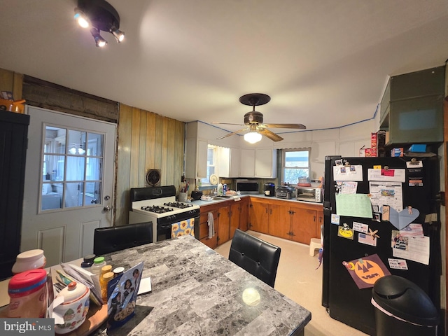 kitchen with brown cabinets, white gas stove, light countertops, freestanding refrigerator, and ceiling fan