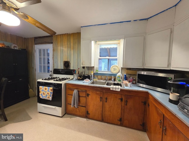 kitchen featuring white gas range oven, stainless steel microwave, brown cabinets, light countertops, and a sink