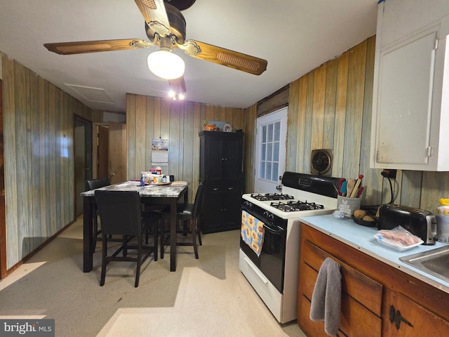 kitchen featuring light countertops, brown cabinets, range with gas cooktop, and wooden walls