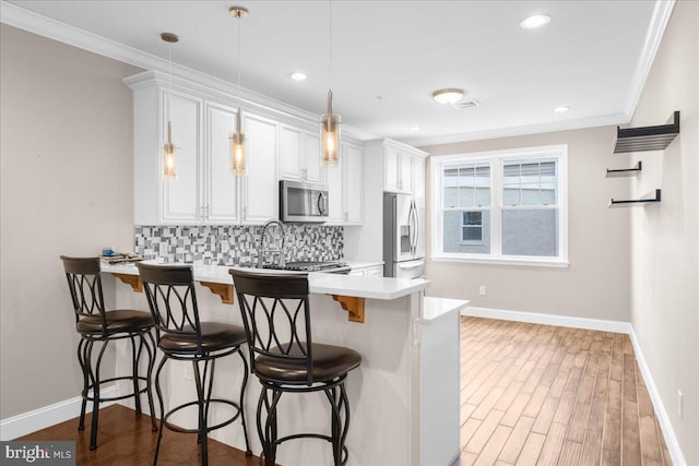 kitchen featuring crown molding, stainless steel appliances, tasteful backsplash, a peninsula, and a kitchen bar