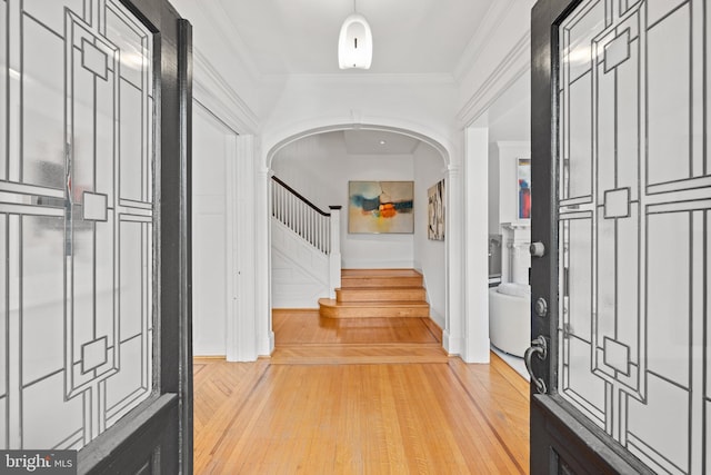 foyer featuring stairway, ornamental molding, arched walkways, and light wood-style floors