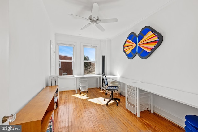 office space featuring crown molding, built in desk, wood-type flooring, a ceiling fan, and baseboards