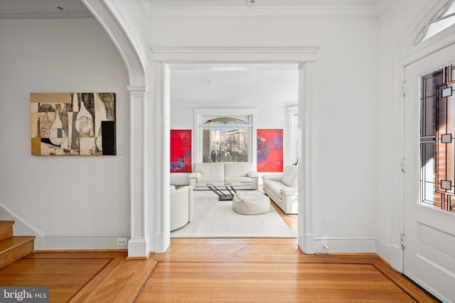 entryway with arched walkways, wood finished floors, stairs, ornamental molding, and decorative columns