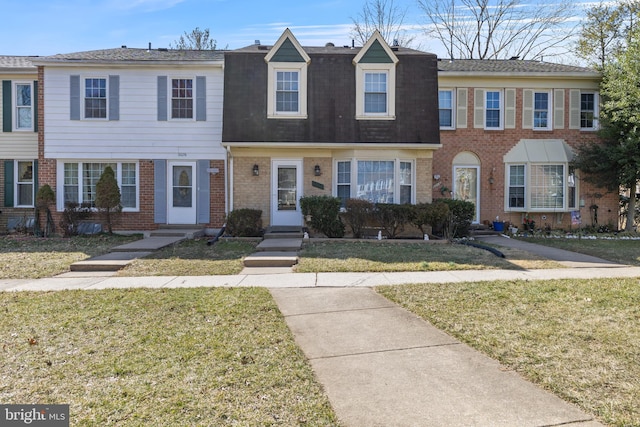 view of property with brick siding, a front lawn, and a shingled roof