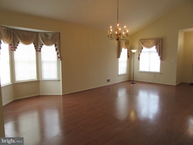 empty room featuring a chandelier, lofted ceiling, wood finished floors, visible vents, and baseboards