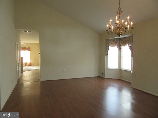 spare room with lofted ceiling, a notable chandelier, visible vents, and wood finished floors