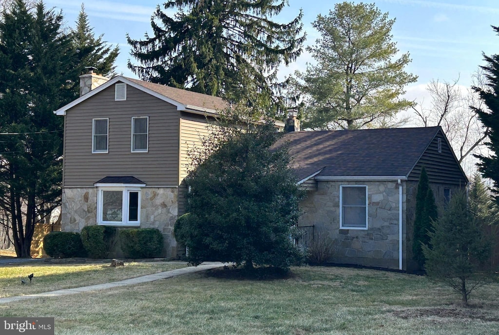 traditional home with a chimney, a shingled roof, a front yard, and stone siding