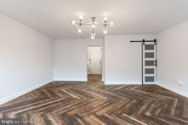 spare room featuring a notable chandelier, a textured ceiling, baseboards, and a barn door