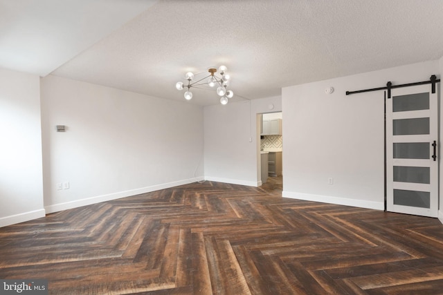 unfurnished room with an inviting chandelier, a barn door, baseboards, and a textured ceiling