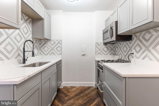 kitchen with stainless steel appliances, gray cabinets, a sink, and baseboards