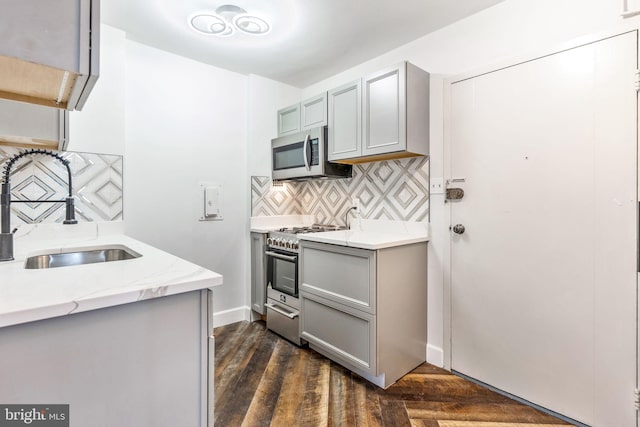 kitchen featuring tasteful backsplash, gray cabinetry, appliances with stainless steel finishes, dark wood-type flooring, and a sink