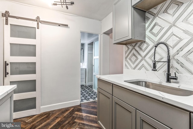 kitchen with dark wood-type flooring, gray cabinets, a sink, and light stone countertops