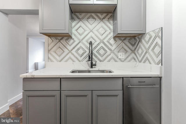 kitchen featuring stainless steel dishwasher, backsplash, gray cabinets, and a sink