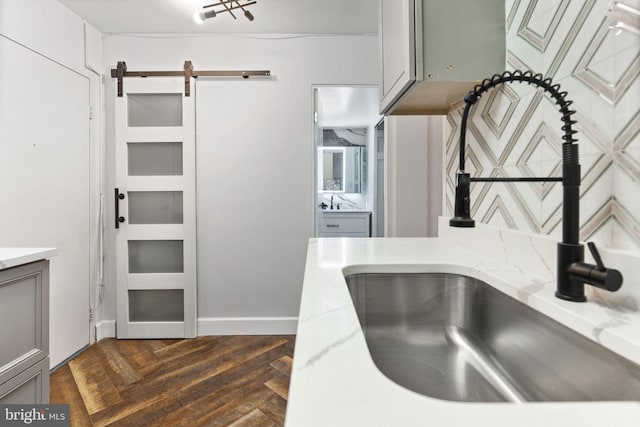 kitchen featuring dark wood finished floors, gray cabinets, a barn door, a sink, and light stone countertops