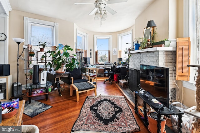 interior space with a ceiling fan, a brick fireplace, and wood finished floors