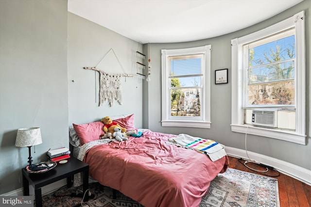 bedroom with cooling unit, baseboards, and wood finished floors