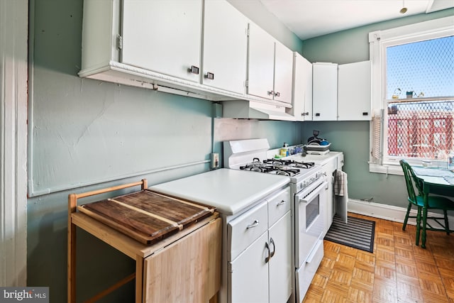 kitchen with under cabinet range hood, white cabinetry, baseboards, light countertops, and white gas range