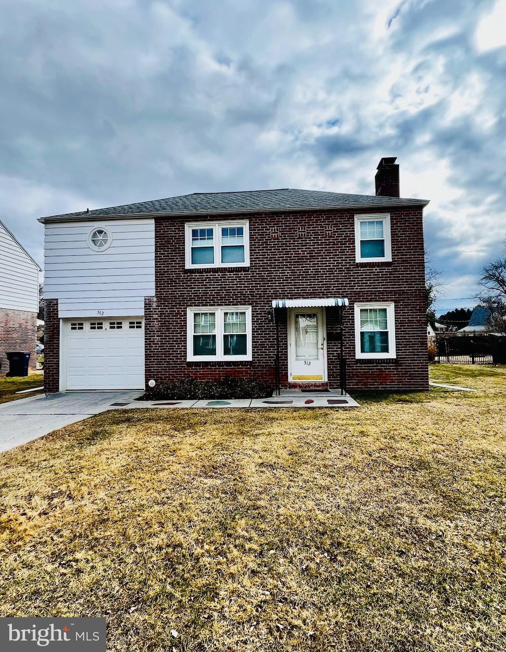 view of front of house with driveway, brick siding, a chimney, and a front yard