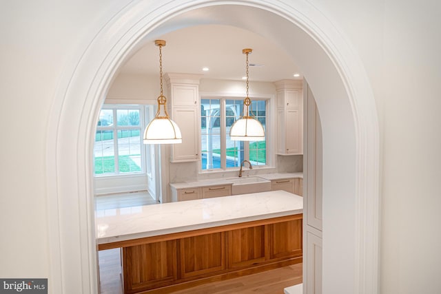 kitchen featuring light stone counters, light wood-style floors, white cabinetry, pendant lighting, and a sink