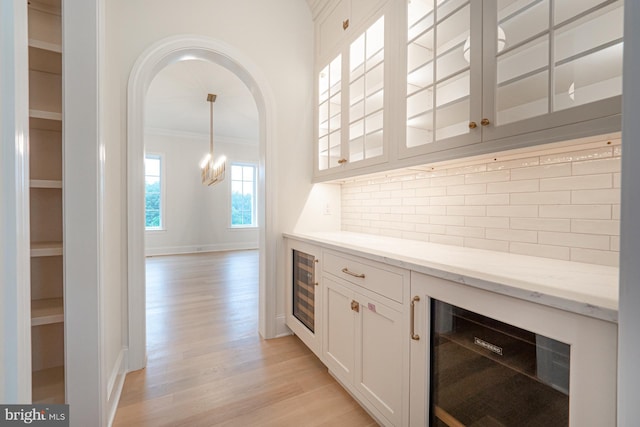 interior space featuring light stone counters, wine cooler, decorative backsplash, light wood finished floors, and glass insert cabinets