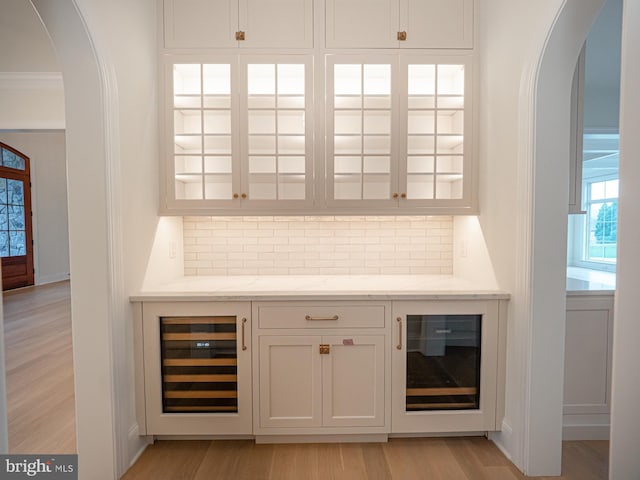 bar featuring light wood-style floors, arched walkways, beverage cooler, and tasteful backsplash