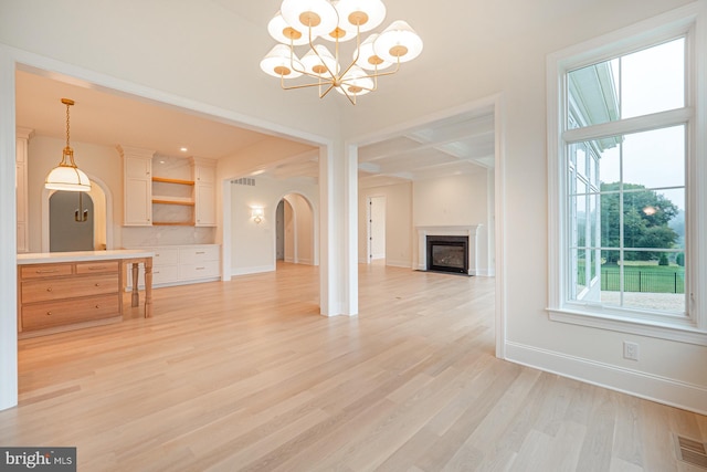 unfurnished living room with baseboards, arched walkways, coffered ceiling, a glass covered fireplace, and light wood-style floors