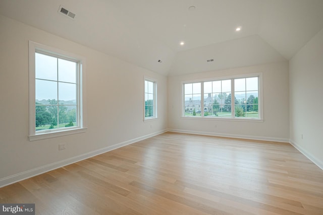 empty room with vaulted ceiling, light wood-type flooring, visible vents, and baseboards