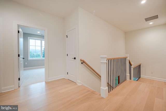 hall featuring visible vents, wood finished floors, and an upstairs landing