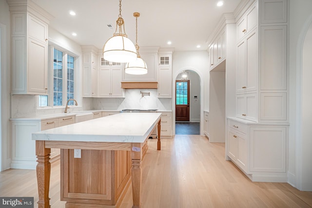 kitchen with arched walkways, a center island, a breakfast bar, light wood finished floors, and glass insert cabinets