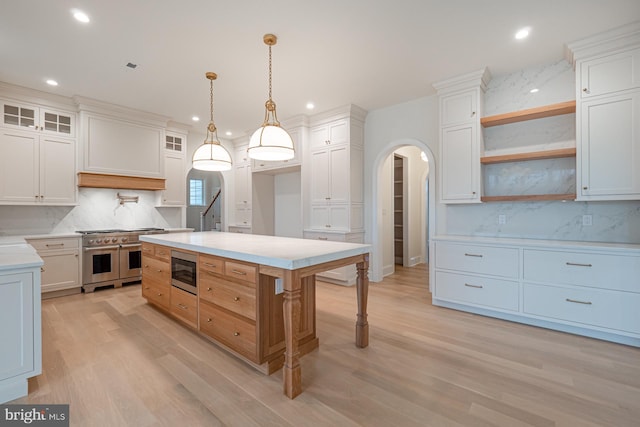 kitchen featuring arched walkways, custom exhaust hood, stainless steel appliances, light countertops, and backsplash