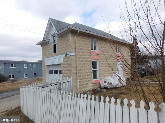 view of side of home with a fenced front yard, a shingled roof, and a garage