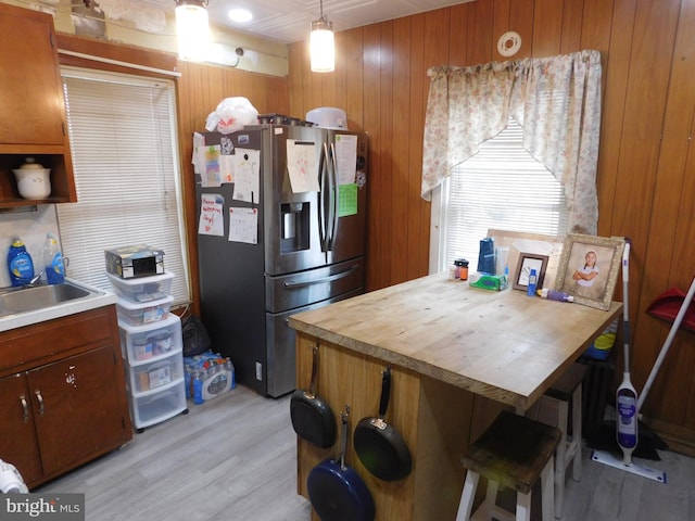 kitchen with light wood finished floors, brown cabinetry, wood walls, stainless steel refrigerator with ice dispenser, and a sink