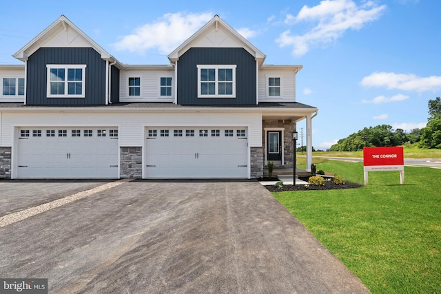 view of front of house with aphalt driveway, board and batten siding, a front yard, a garage, and stone siding