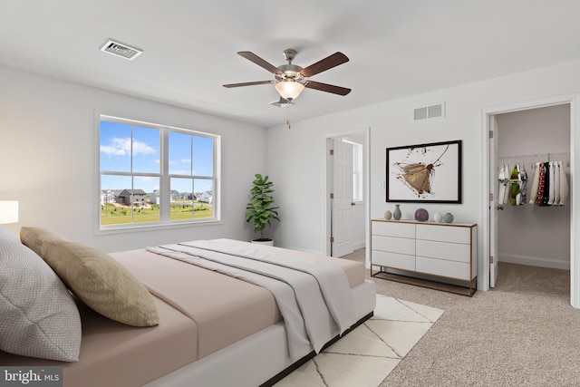 bedroom featuring a ceiling fan, a walk in closet, light colored carpet, and visible vents