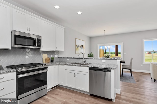 kitchen featuring stainless steel appliances, light wood-style floors, white cabinets, a sink, and a peninsula