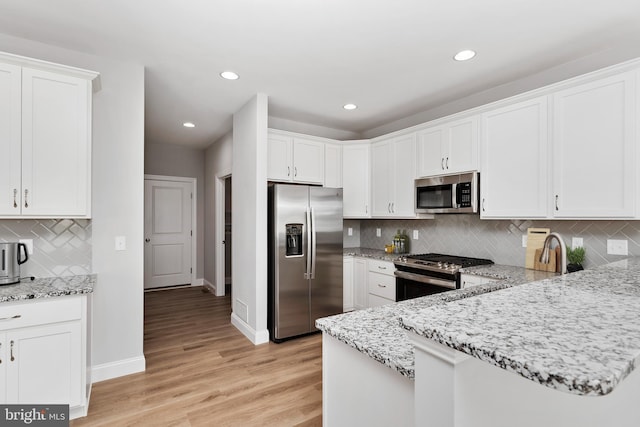 kitchen featuring appliances with stainless steel finishes, white cabinets, light wood-style floors, and light stone counters