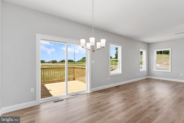 unfurnished dining area featuring an inviting chandelier, visible vents, baseboards, and wood finished floors