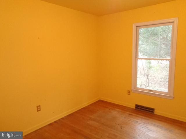 spare room featuring wood finished floors, visible vents, and baseboards