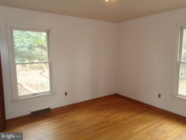 empty room with light wood-style flooring, visible vents, and baseboards