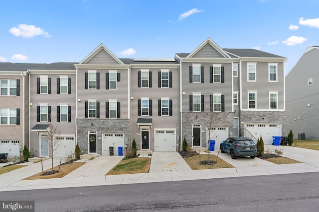 multi unit property featuring stone siding, driveway, an attached garage, and solar panels