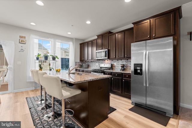 kitchen featuring decorative backsplash, appliances with stainless steel finishes, a sink, dark brown cabinets, and light stone countertops