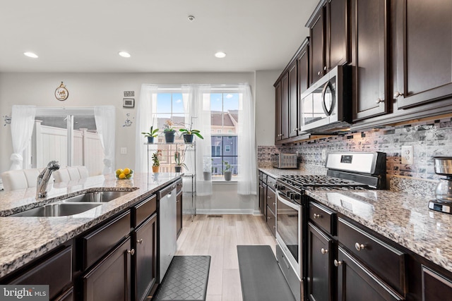 kitchen with light stone counters, tasteful backsplash, appliances with stainless steel finishes, a sink, and dark brown cabinets